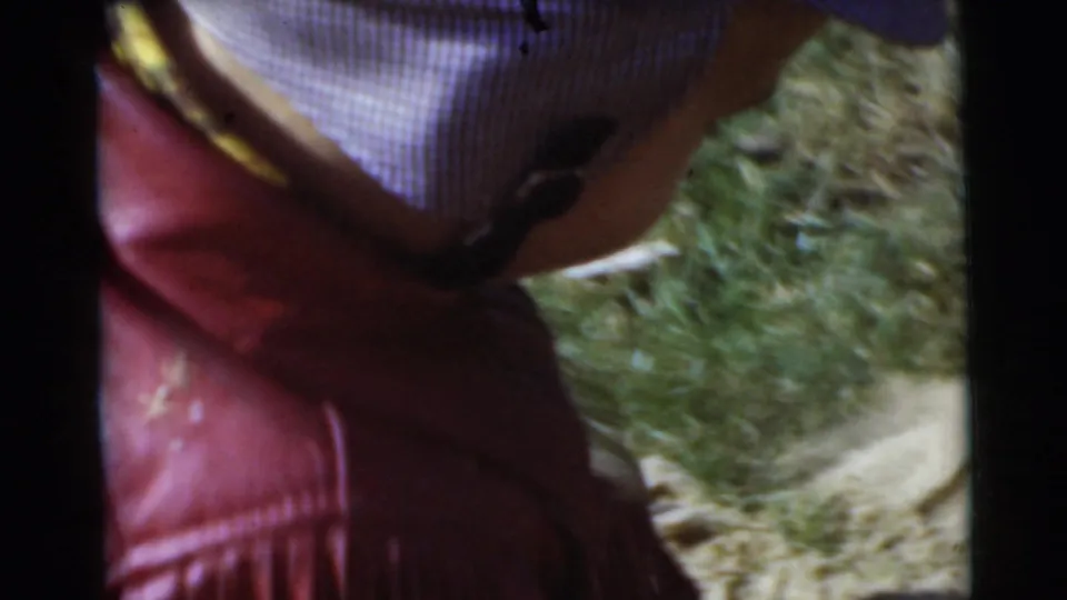 In supported 1956 Miami home-movie footage, a small child is seen from behind wearing a red fringed jacket and striped cap on a lawn.