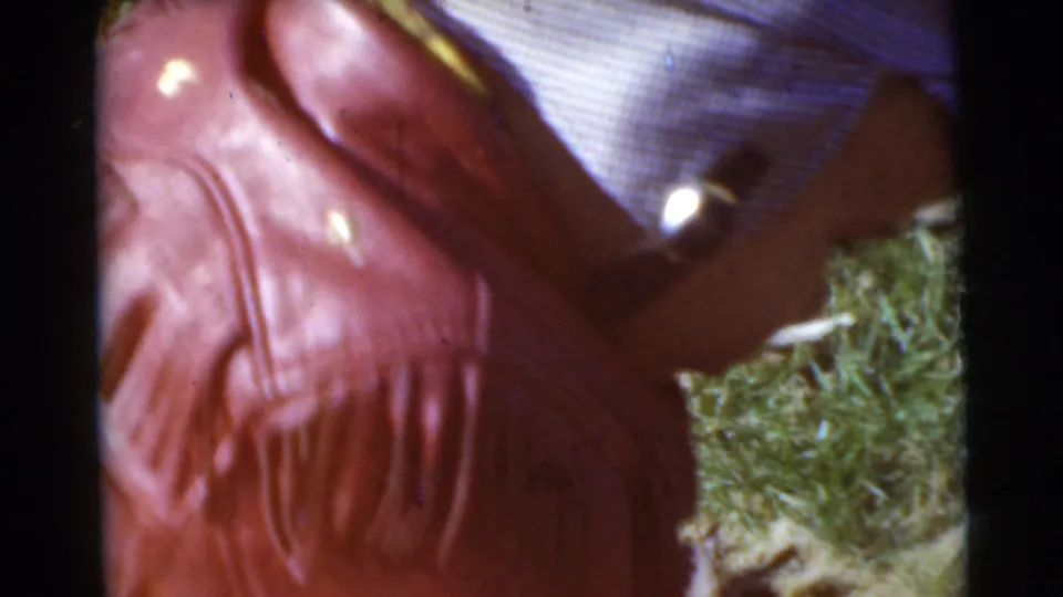 The child in the red fringed jacket and striped cap appears to bend or move forward on the grassy Miami lawn in this 1956 home-movie frame.