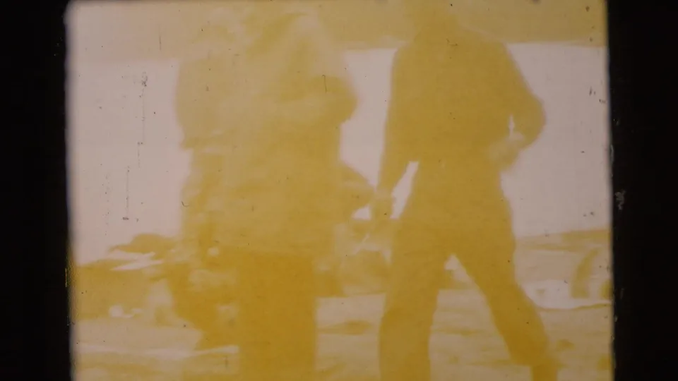 Yellow-shifted 1956 Miami home-movie frame with two bundled men silhouetted near a lakeside setting.