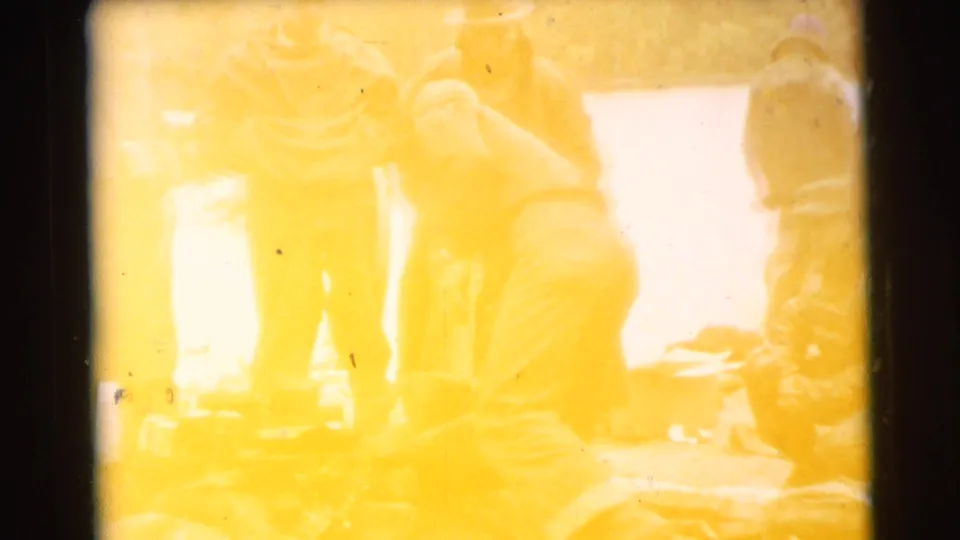 Overexposed 8mm frame from the Miami campfire scene, with men grouped near a small fire and outdoor gear.