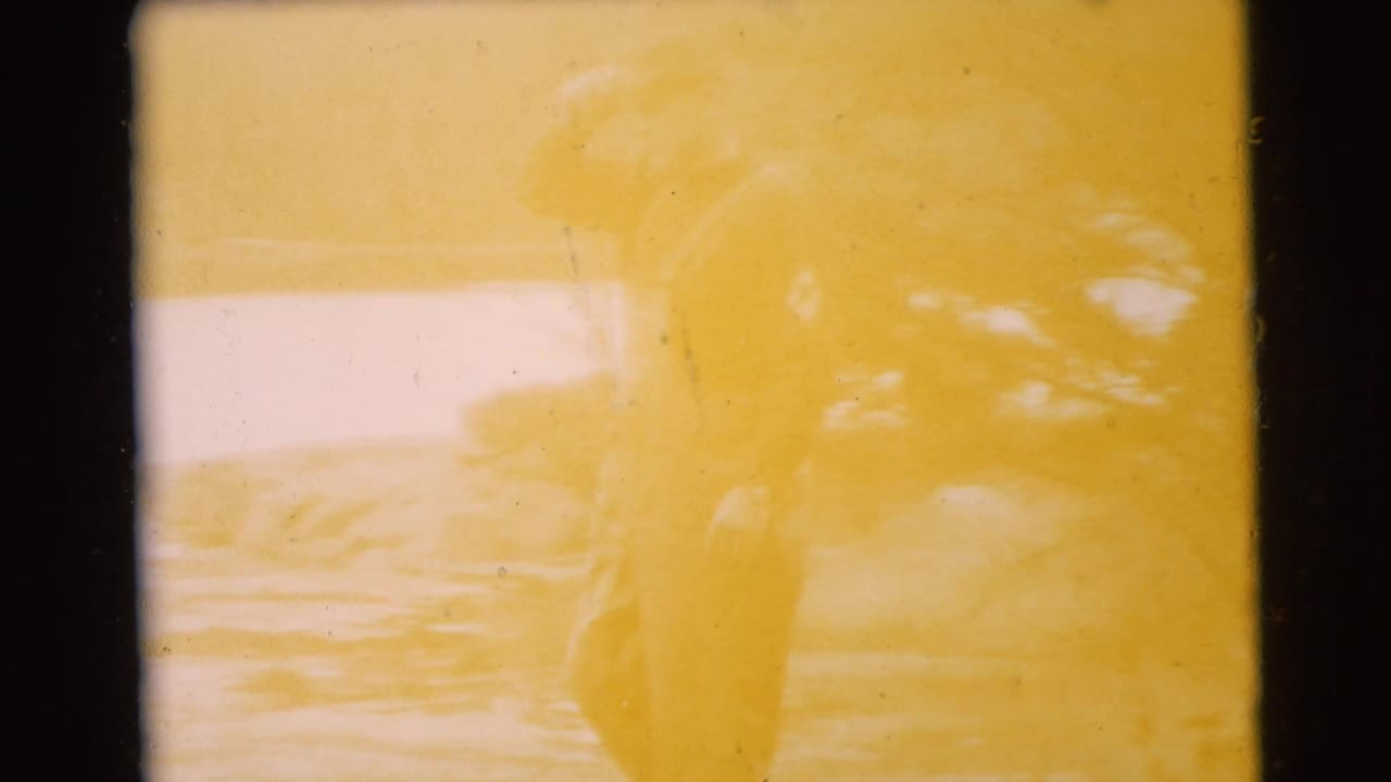 Yellow-tinted frame with a standing figure partly obscured by exposure and foliage.