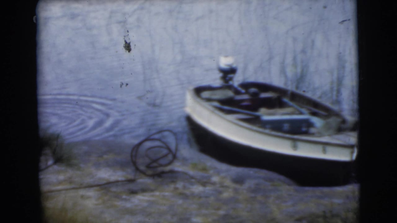 Small motorboat pulled up beside rippling lake water and rocky shoreline.