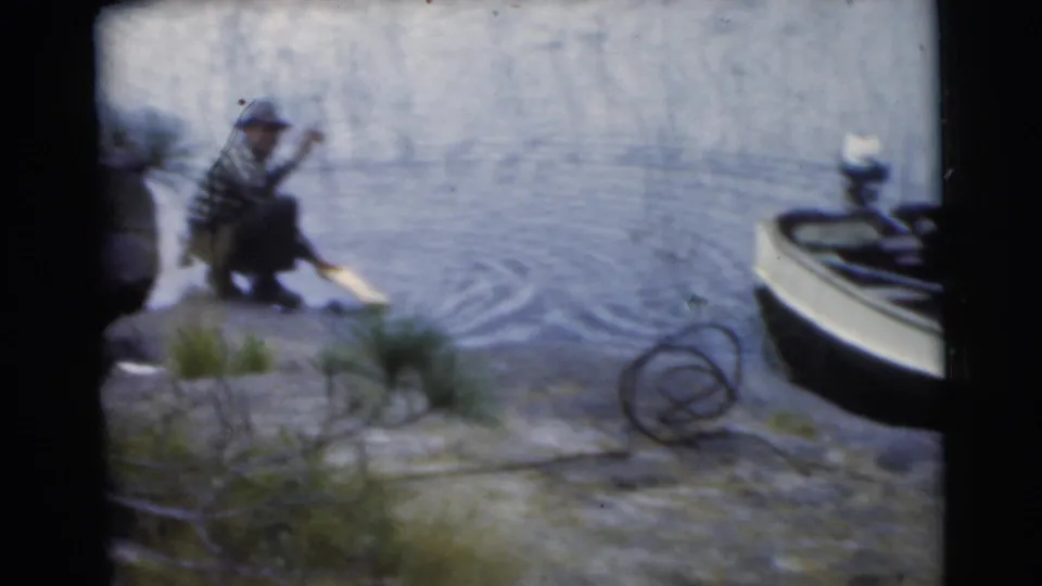 1956 Miami frame showing a man crouched at the lake edge, reaching toward the water with a motorboat nearby.