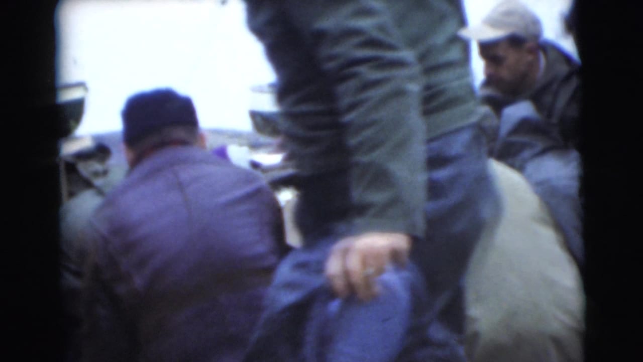 Men gather closely near an outdoor food area beside water.