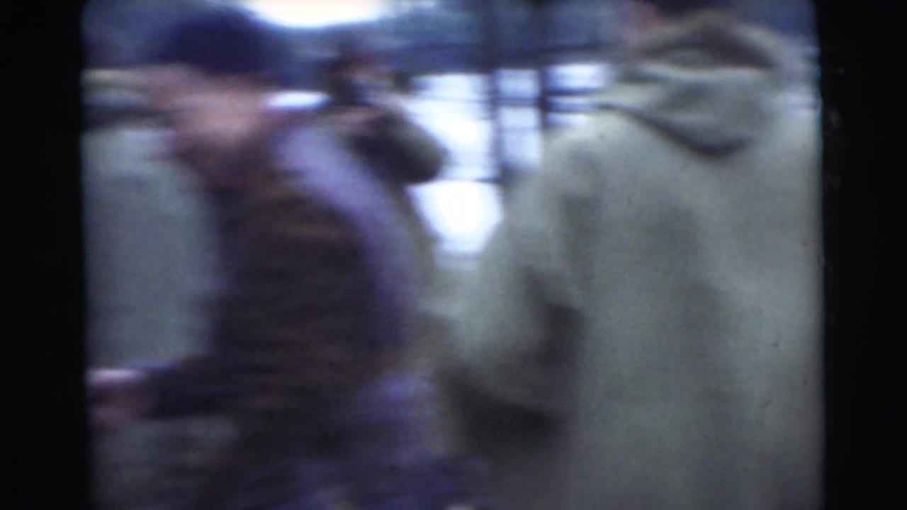 Soft 1956 Miami 8mm frame showing bundled men near water, with strong motion blur and dark film borders.