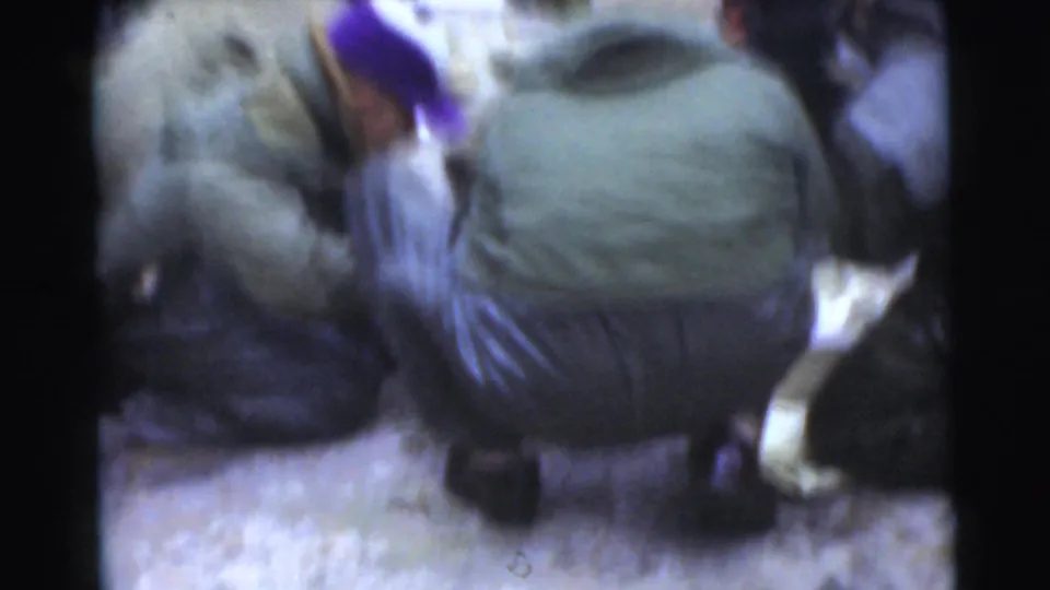 Miami 1956 home-movie frame showing a crouching man in a coat with other bundled figures close around him.