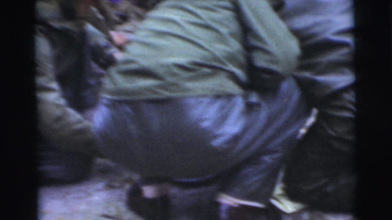 Men in dark coats stand close together, with one figure in a green shirt seen from behind.