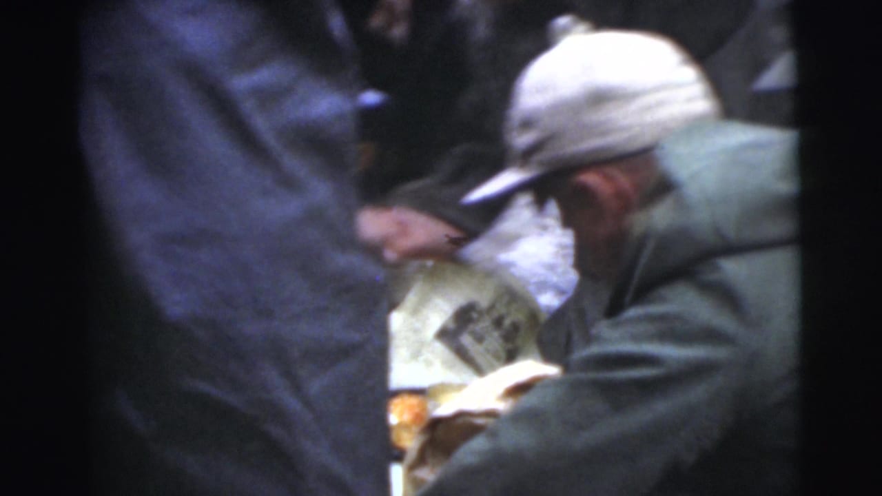 A man in a white cap bends near other men, with food or paper partly visible between them.