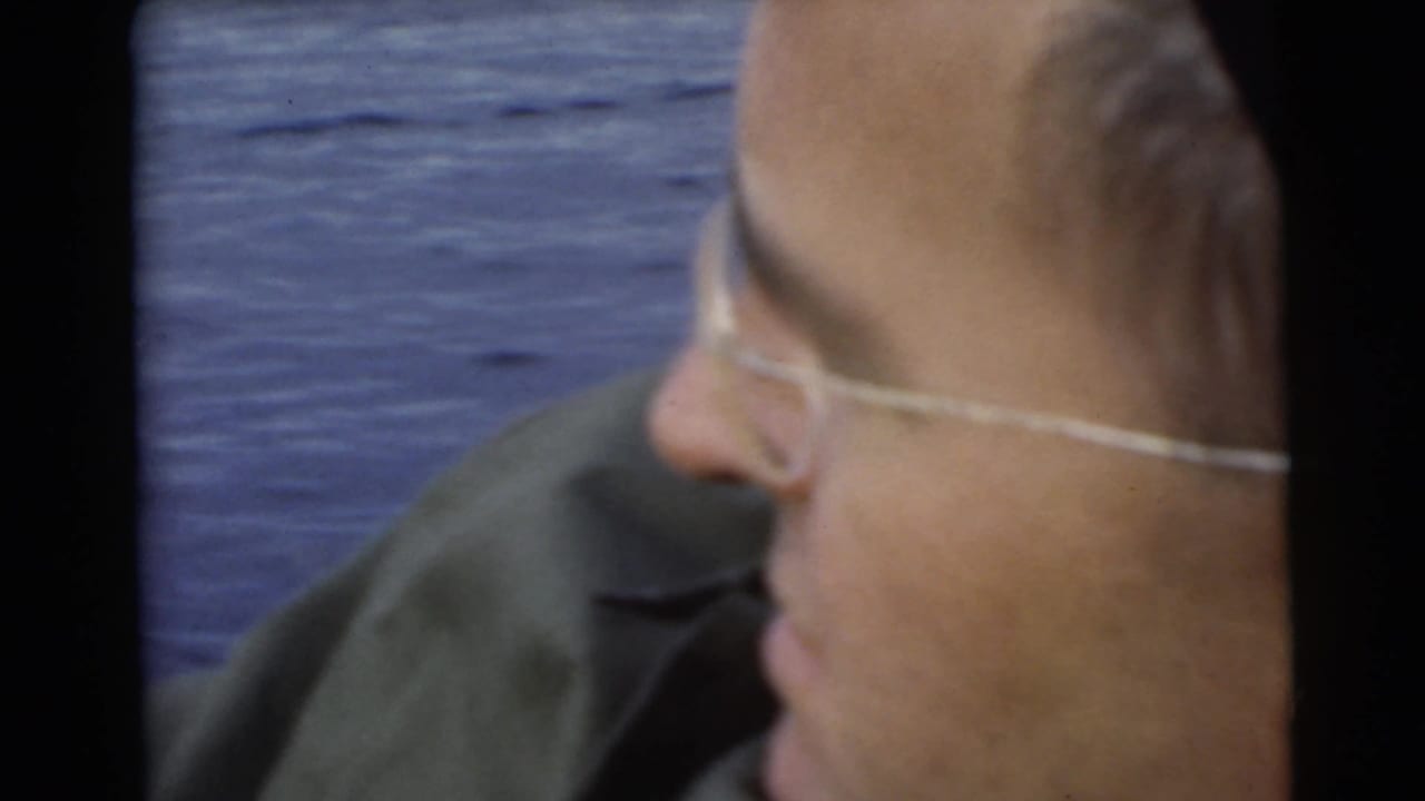 Man in glasses seen in side profile beside blue lake water.