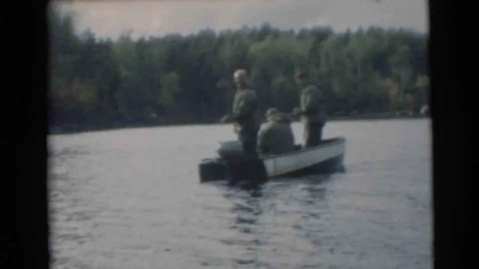 Three men fish from a small motorboat on a wooded lake in 1956 Miami, Florida home-movie footage.