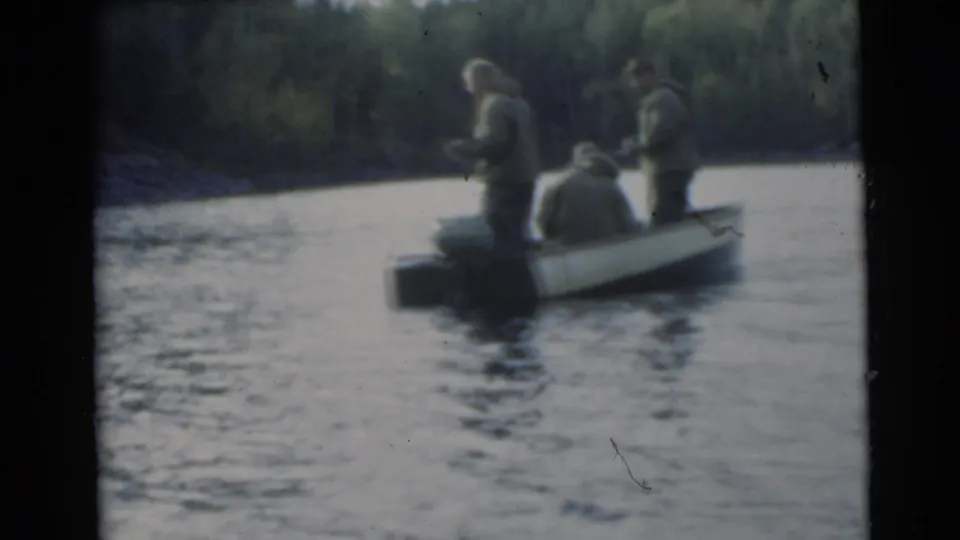 A small outboard boat carries three men fishing on a lake, with trees lining the shore behind them.