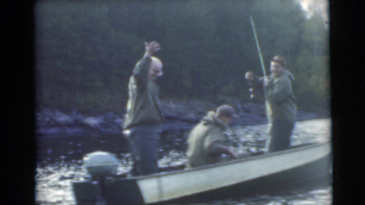 Man at the stern lifts a fish while two other men remain in the boat.
