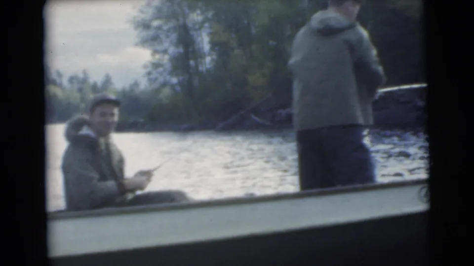 1956 Miami-area 8mm frame with a seated man facing the camera and another man fishing from the stern of a small boat.