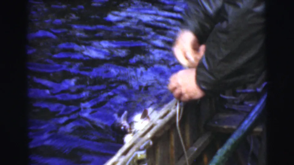 Close 8mm frame from the fishing outing shows hands working near rope or gear at the side of a small boat on rippling water.