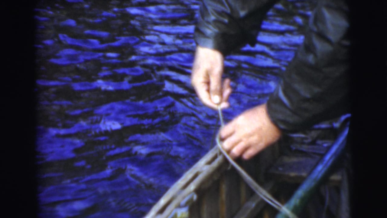 Hands pulling fishing line beside the edge of a small boat on rippled blue water.