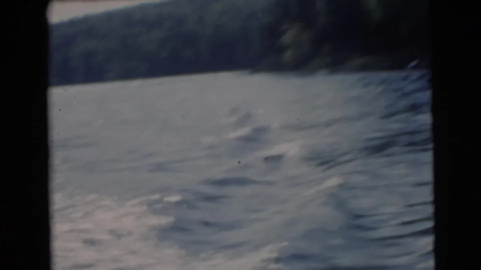 Faded 8mm frame of a Miami lake with dark shoreline, rippled water, and handheld home-movie framing.