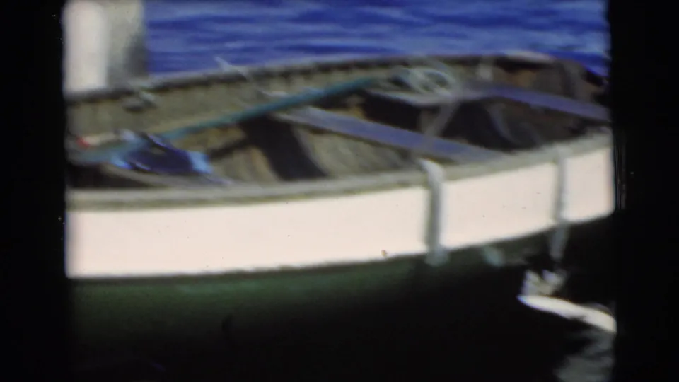 The rowboat interior shows oars and rope while the caught fish hangs partly visible near the side in the Miami home-movie footage.