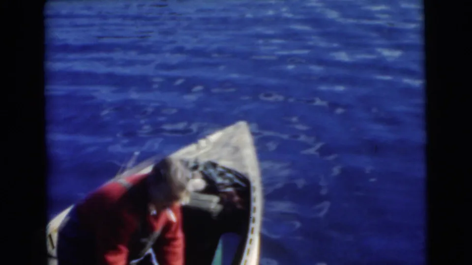1956 Miami home-movie frame showing a man in a red shirt leaning over the bow area of a wooden boat on open water.