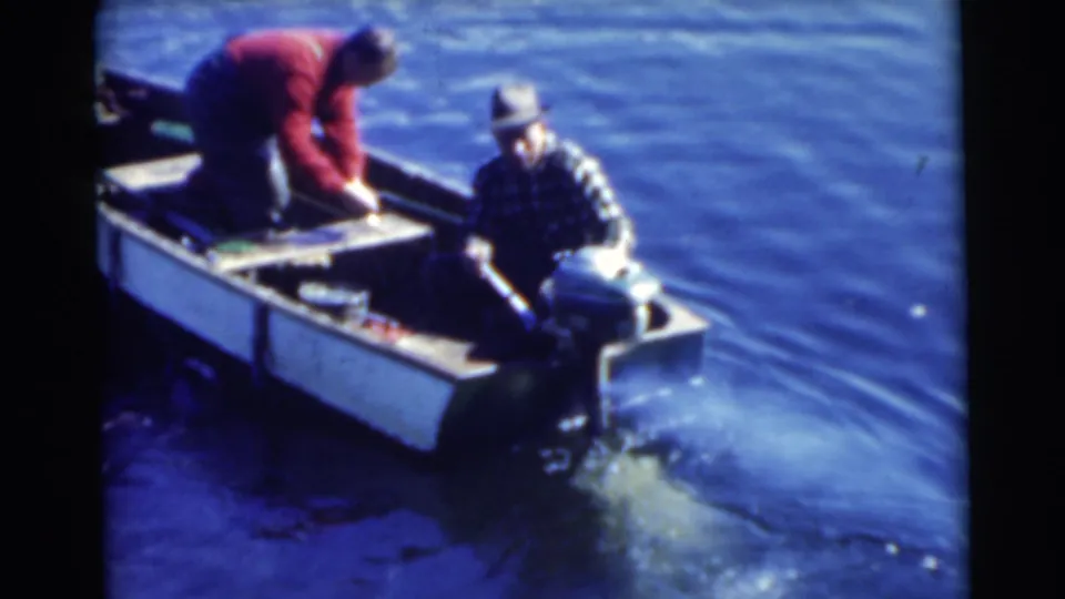 1956 Miami frame of a small motorboat underway or idling, with a seated older man by the outboard motor and a standing man in a red shirt.
