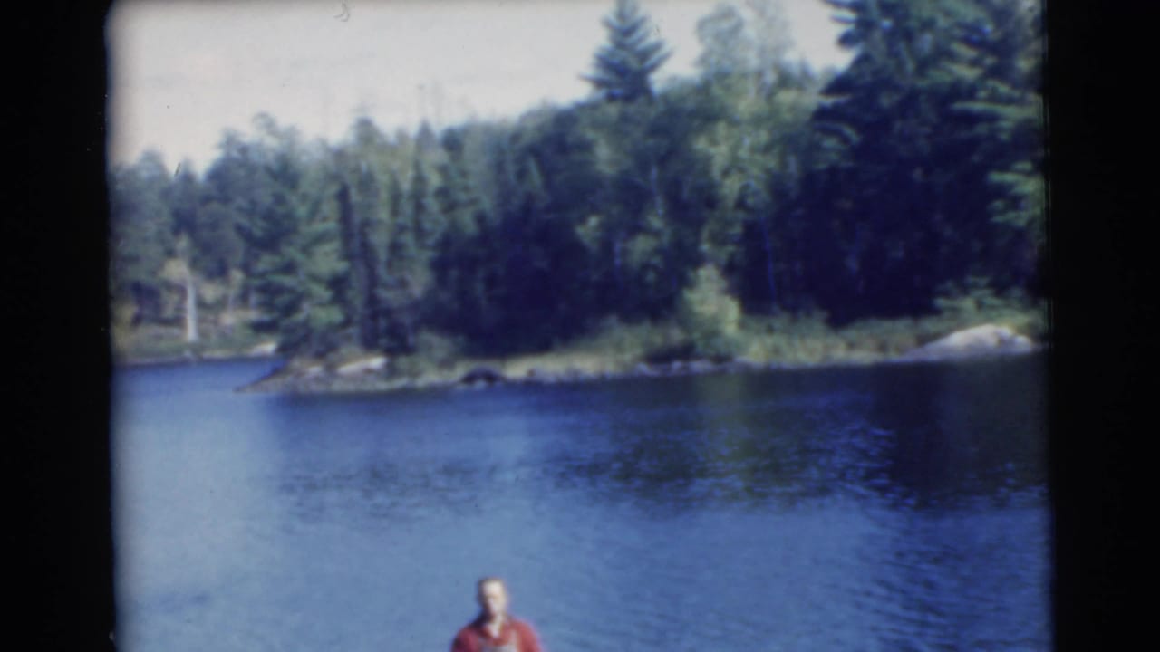 Blue lake and wooded shoreline with a man in a red shirt partly visible at the bottom of the frame.