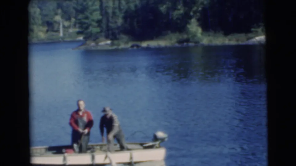 Two adult men in a small motorboat on a Miami-area lake in 1956, with one in red standing and another near the outboard motor.