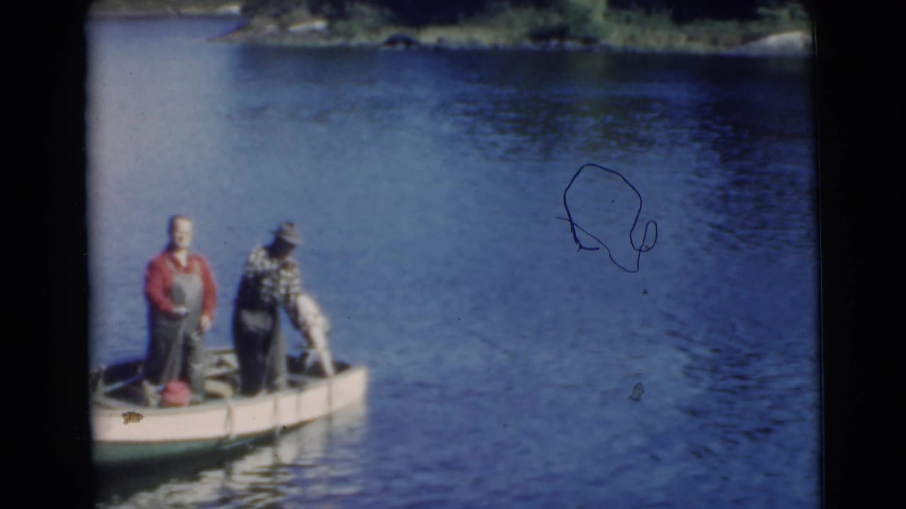 Two men in a small boat work near a large fish beside the boat on lake water.