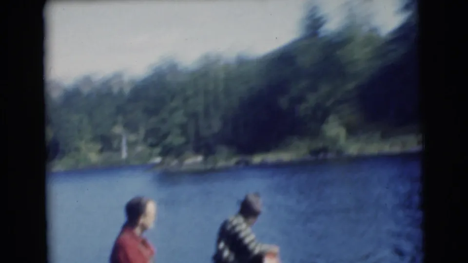 Soft 8mm frame from the 1956 Miami fishing clip, showing two men in a small boat with a wooded shoreline behind them.
