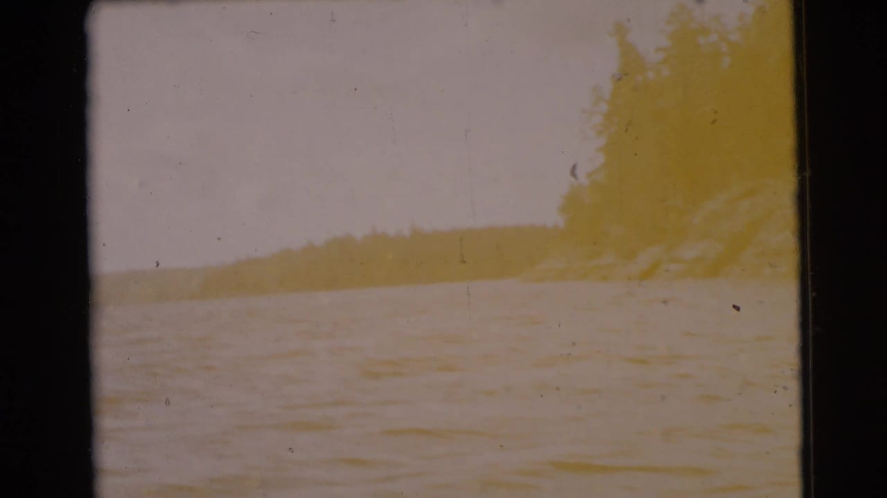 Overexposed lake view with distant tree-lined shore and dark 8mm frame edges.