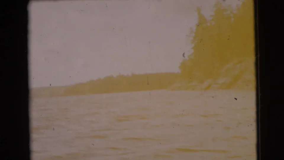 1956 8mm boat-view footage shows a bright, faded lake surface with a distant wooded shoreline and visible film border.