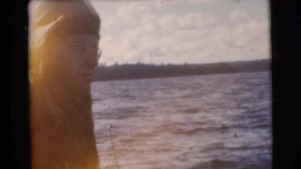 1956 8mm Miami frame with a person in profile near the lakeside, backed by water and a distant tree-lined shore.