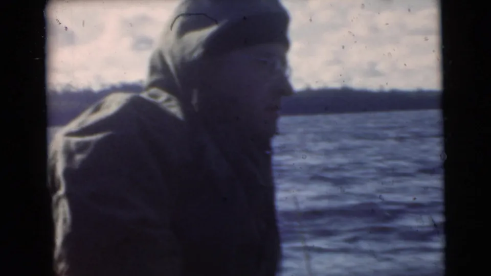Close view of an adult man in a hooded jacket and glasses near water, from a 1956 Miami-area home-movie clip.