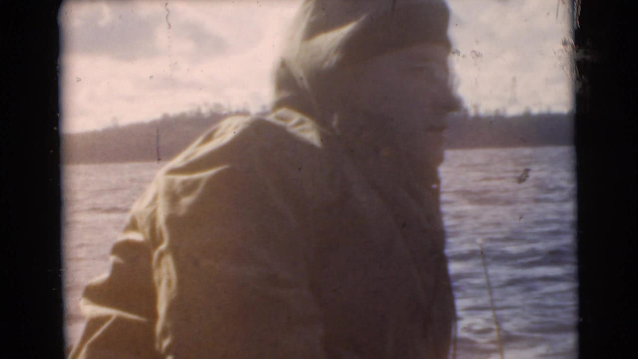 Close view of a man in a hooded jacket on or near a boat with water behind him.