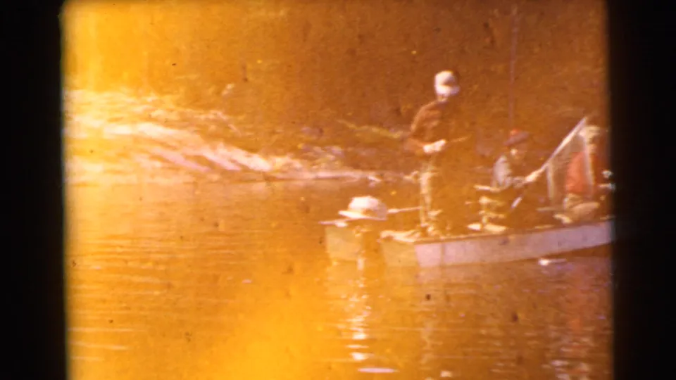 Three adult men appear in a small motorboat near a wooded shoreline during the 1956 Miami fishing scene.