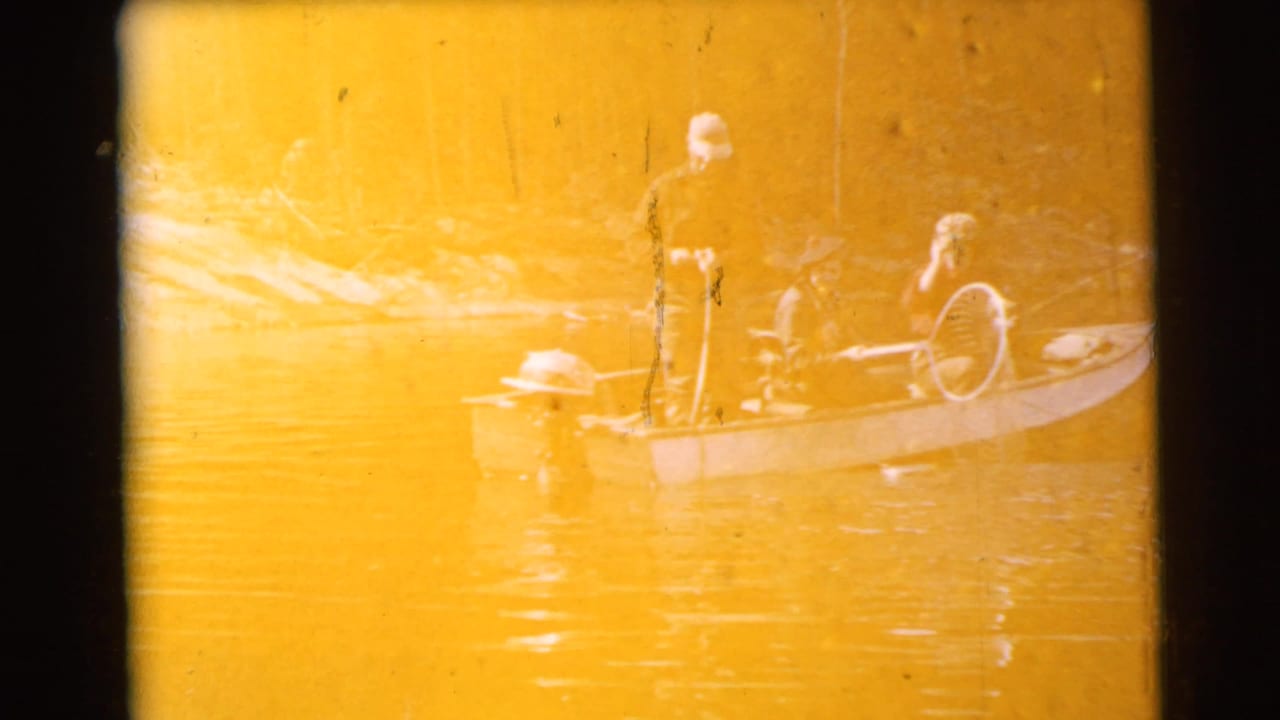 Two adults in a small boat on calm water, heavily faded by warm yellow exposure.