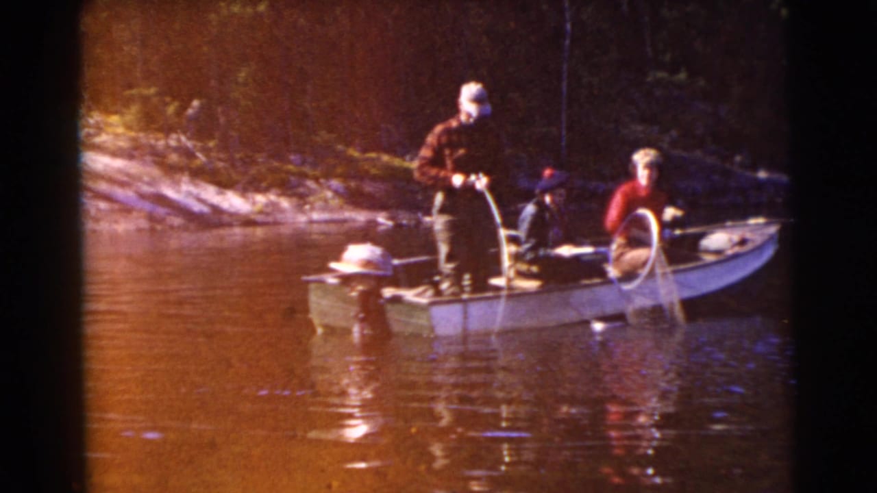 Two adults in a small motorboat, one standing near the stern and one seated at the bow with fishing gear.