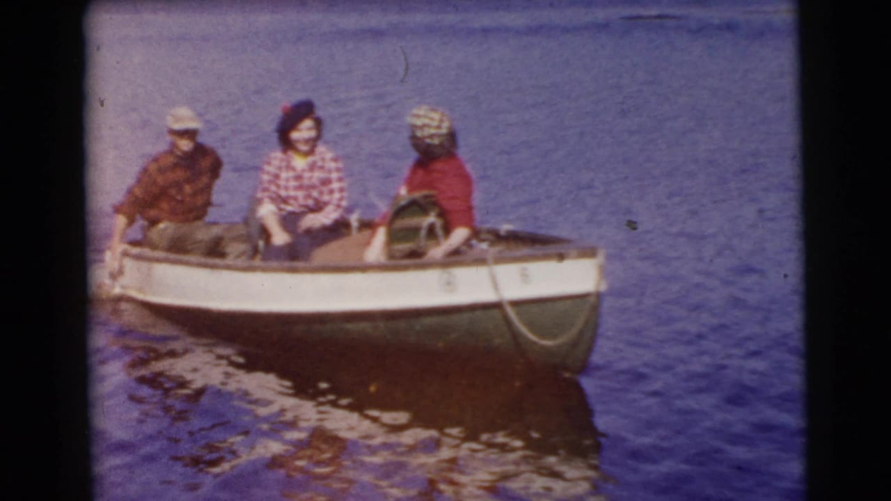 Three adults sit in a small open boat on calm water.