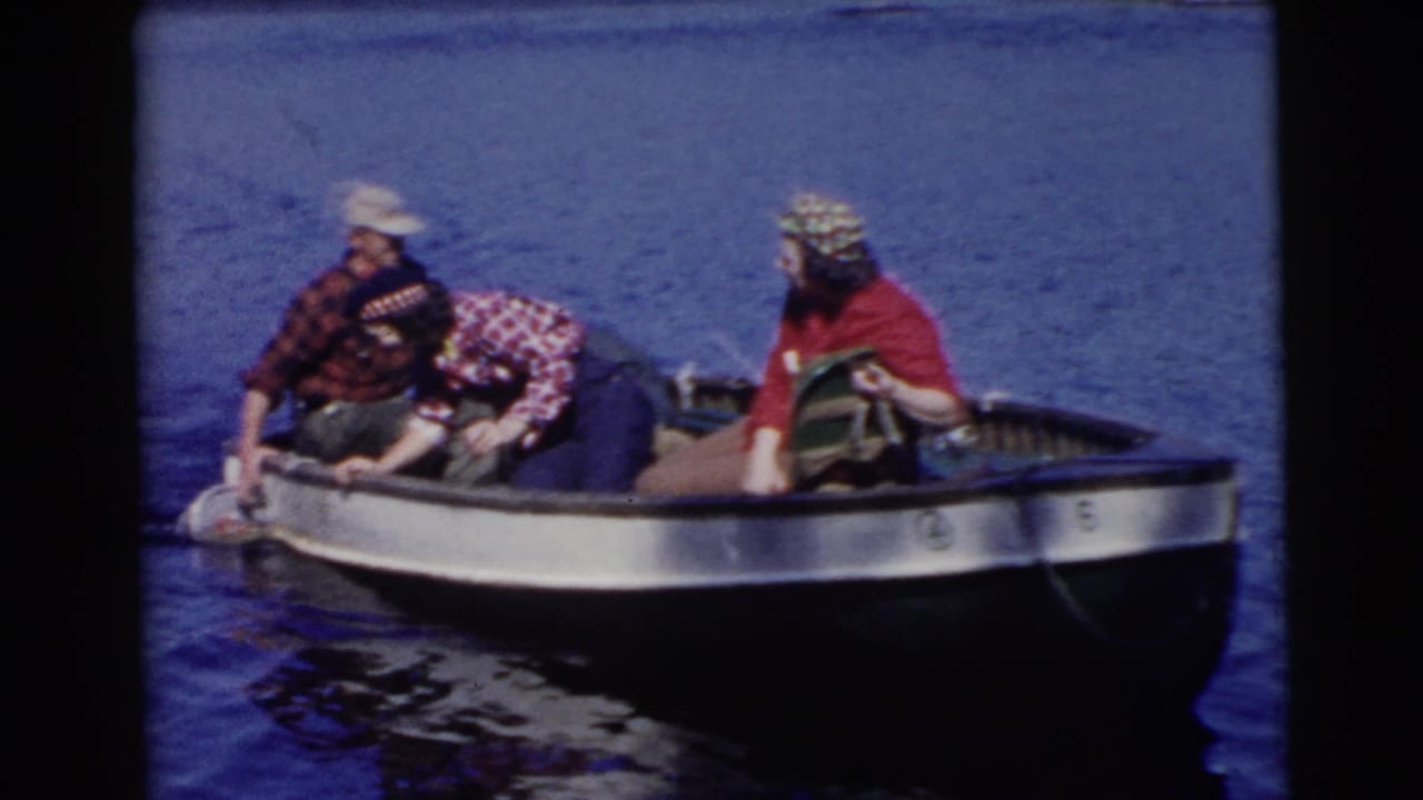 A man and two women sit in a small boat, with one woman leaning over the side.