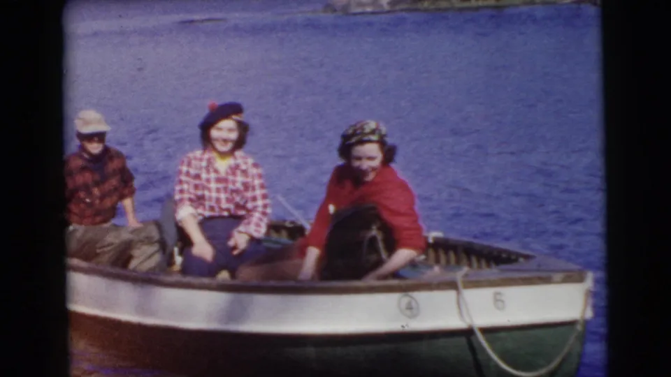 Three adults in a small boat smile toward the camera during a 1956 Miami home-movie boating outing.