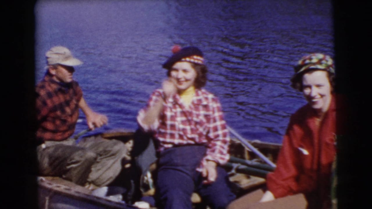 A man and two women sit in a small boat on a lake, with one woman smiling toward the camera.