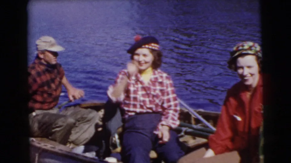 Adults in a small boat on a Miami lake in 1956, with plaid clothing, fishing gear, and bright blue water behind them.