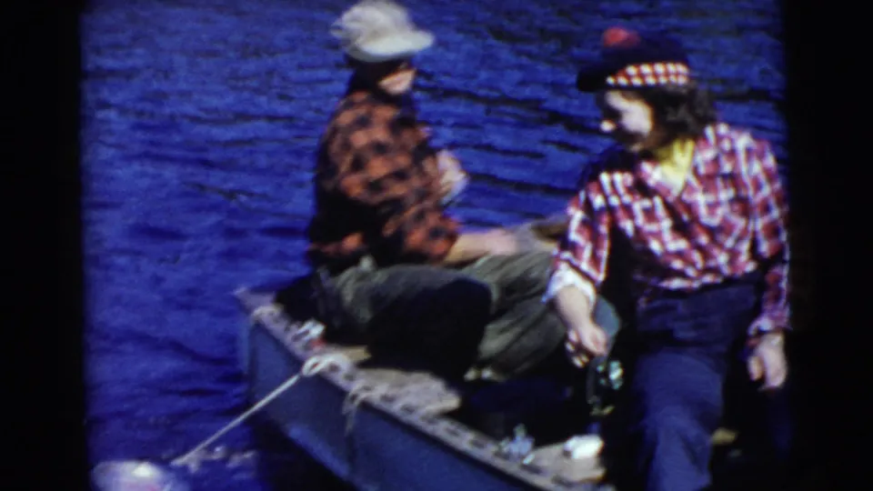 1956 Miami lake outing frame showing a man and woman in a small boat, with the woman moving beside fishing gear or a line.