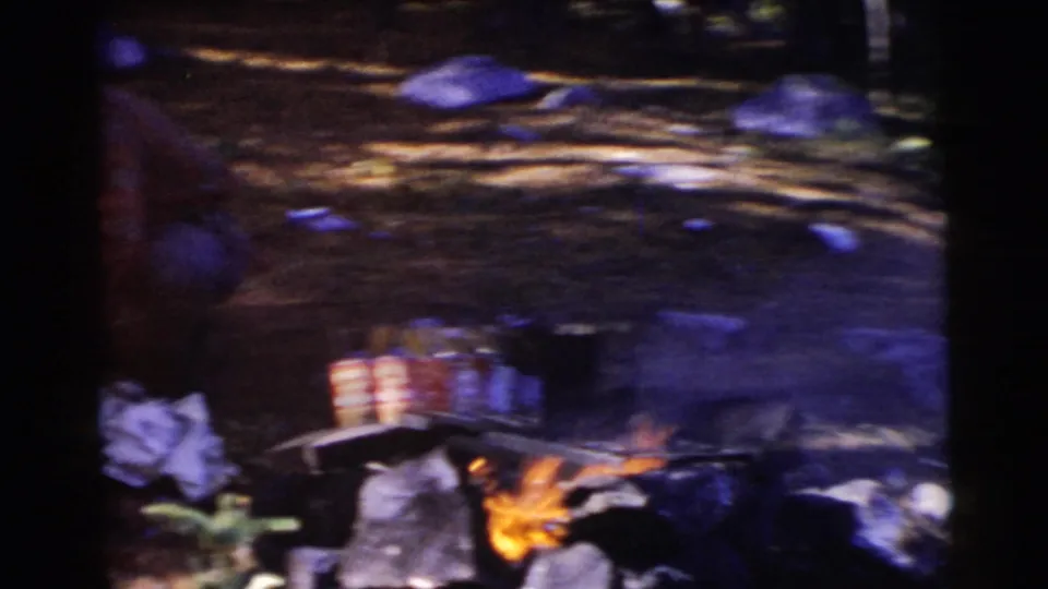 A small outdoor fire burns near scattered items on the ground in a 1956 Miami home-movie frame.
