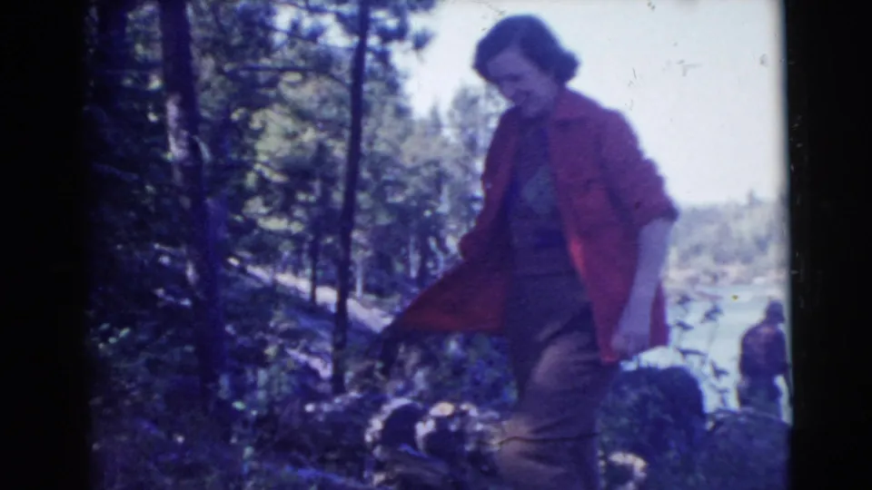 A closer 1956 Miami frame shows the woman in a red jacket among trees and brush with water beyond.