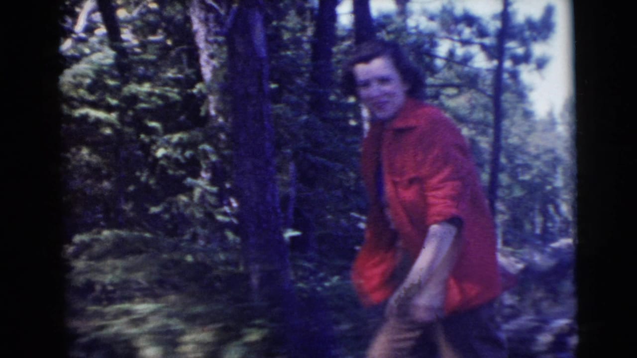 Woman in a red jacket walking through a wooded area.