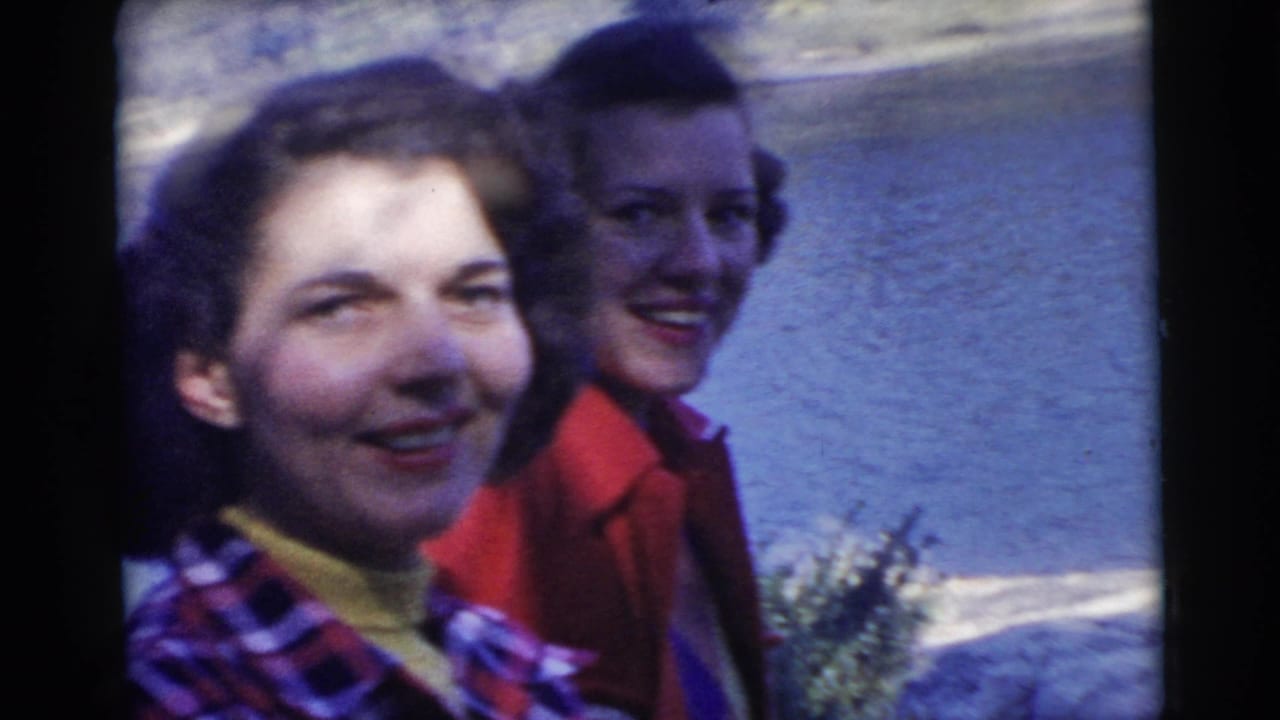 Two women smiling beside a lake, one in a plaid shirt and one in a red jacket.