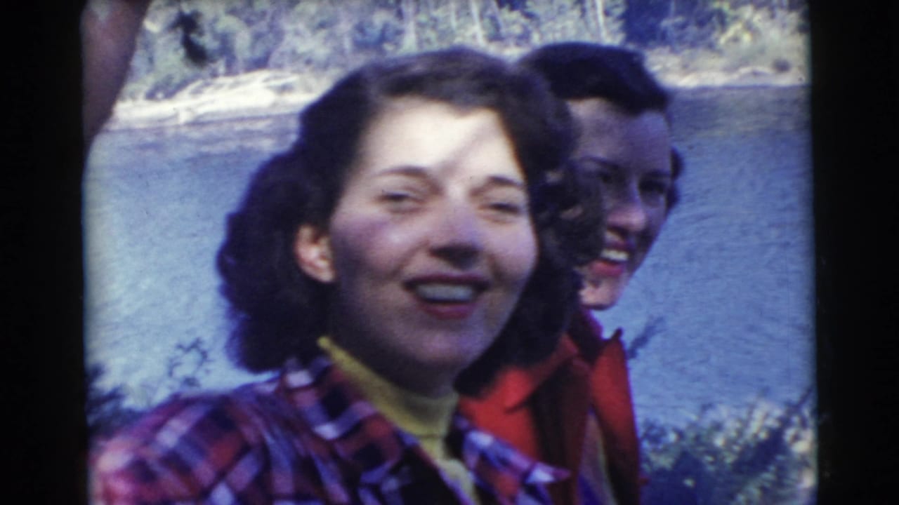 Two women laughing close to the camera with lake water and trees behind them.