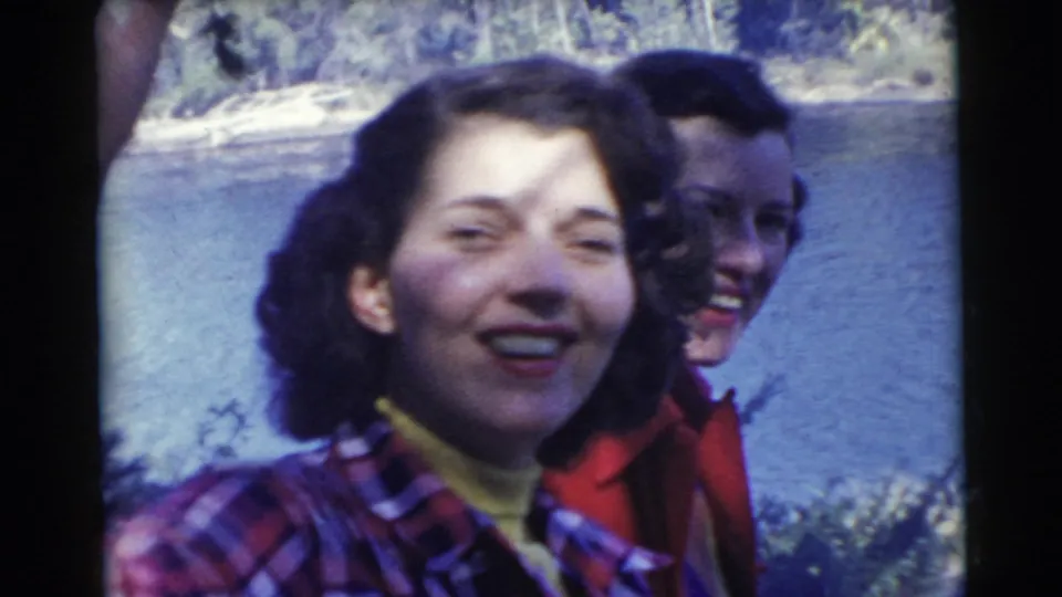 Two women laugh close to the camera by a lake in the supplied 1956 Miami home-movie footage.
