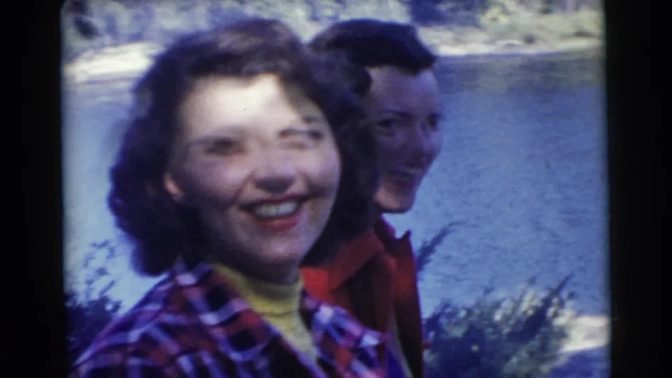 A close lakeside home-movie frame shows two women smiling and laughing in metadata-supported 1956 Miami.