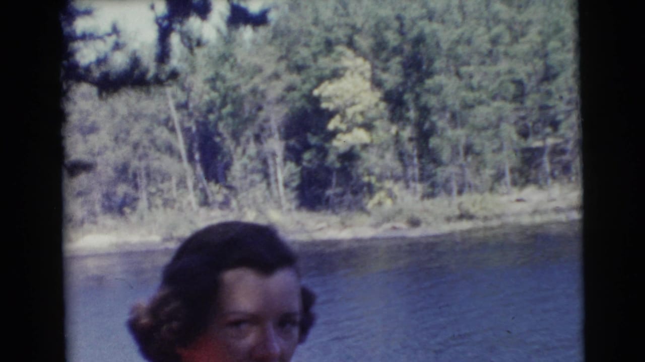 Partially visible woman by a lake with trees along the far shore.
