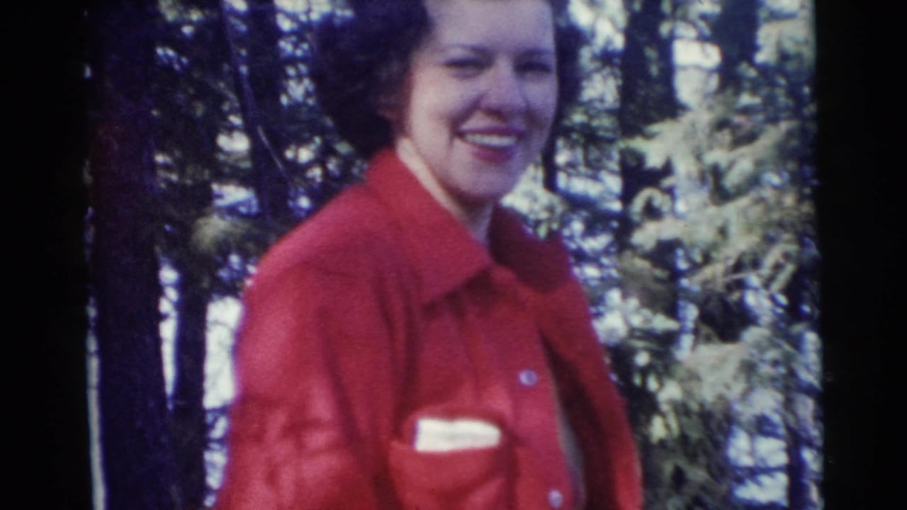 Smiling woman in a red jacket standing among trees.